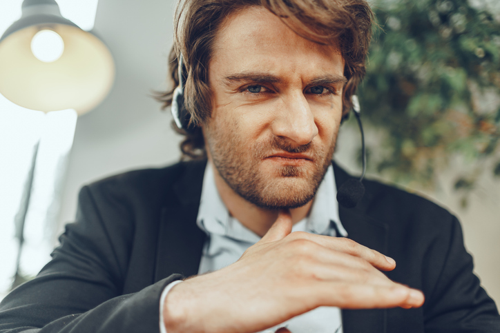 Close up portrait of an angry businessman with headset having stressful online conversation
