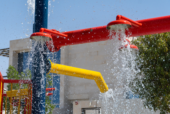 Three red spray water park sprinklers spraying water below for children's summer fun.