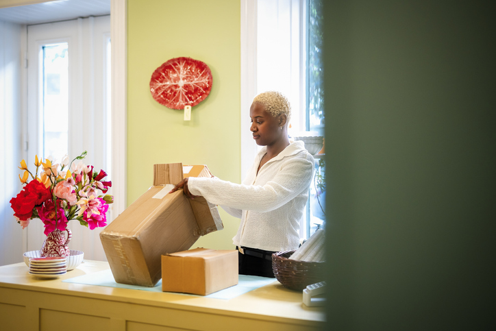 Female owner packing cardboard box standing at checkout in home decor shop